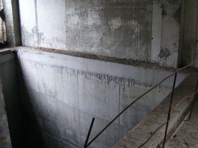 Perete de beton aparent cu urme de cofraj și o ghenă în planșeu.