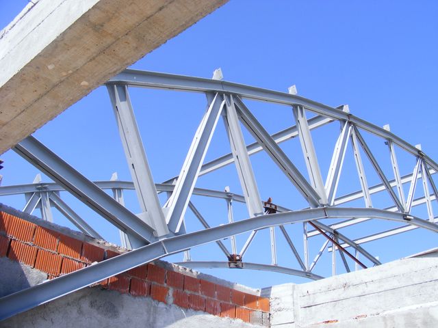 Arc metalic cu zăbrele pe fondul cerului, deasupra unui zid de cărămidă