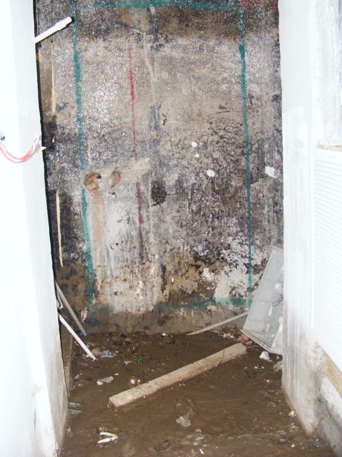 Perete de beton cu marcaje pentru golul de ușă, cu pământ și resturi pe pardoseală